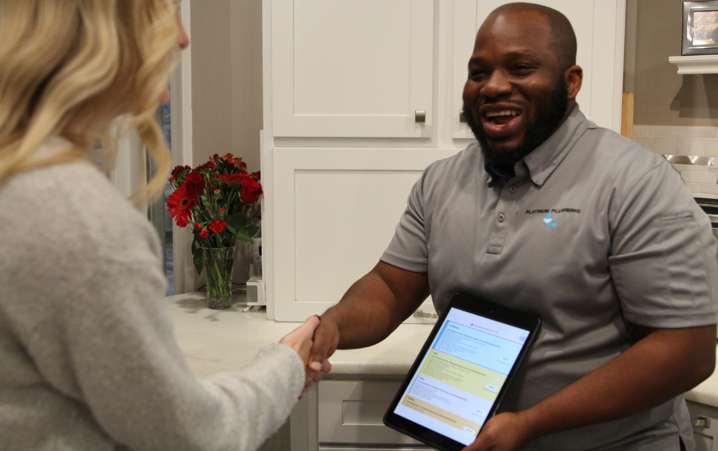 Plumbing technician shaking hands with a homeowner while presenting service options on a tablet in a modern kitchen